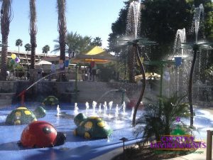 Large custom landscaped splash pad with childrens fountains and colorful water fall structures and turtles surrounded by seating area and cabanas