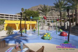 Large custom landscaped splash pad with childrens fountains and colorful water fall structures and turtles surrounded by seating area and cabanas
