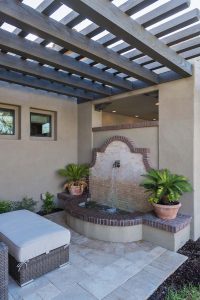 Large Spanish fountain made of brick with unique metal water nozzle under custom pergola on a custom landscaped side yard