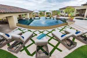 Custom landscaped backyard with a zero edge pool near a covered patio and potted plants