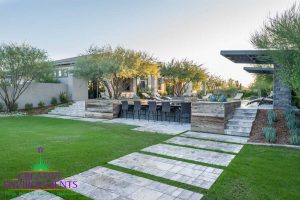 Large backyard grassy area with desert landscape with brick paver steps up to the patio