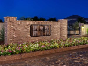 Custom landscape and hardscape community entrance with brick paved road and custom rustic sign