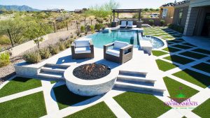 Squared artificial grass pattern in backyard around custom swimming pool, fire pit, and lounge area with putting green surrounded by desert