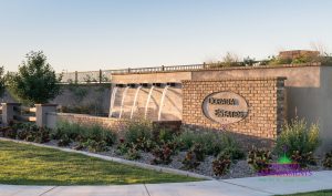 Custom landscape and hardscape community entrance with large brick structure with custom metal art chains and potted plants with water features surrounded by grass and desert landscape