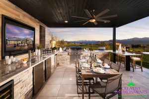 Custom backyard desert landscape with large covered patio with an outdoor kitchen and bar area with outdoor dining and television