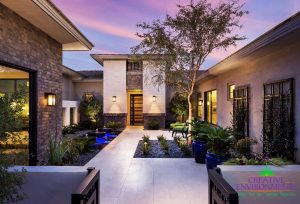 Custom landscape home entryway with desert plants and trees with climbing plants, a water fountain with lights, and lounge area