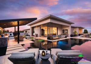 Custom backyard landscape with zero edge pool open to the homes living room with floating steps, lounge area, wall water feature, and outdoor kitchen and dining