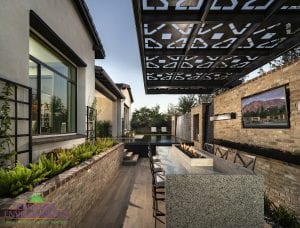 Custom outdoor landscape in Arizona backyard area with narrow dining table seating with a tabletop fireplace and custom metal pergola