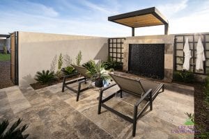 Custom backyard landscape with side yard lounge area under a pergola near a black pebble water fountain