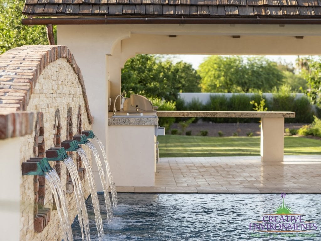 Custom outdoor landscape showing a decorative Chicago brick wall about the swimming pool with waterfall water features near a covered patio