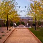 Custom backyard design with bocce ball court, string lights and square fire pit with outdoor seating area.