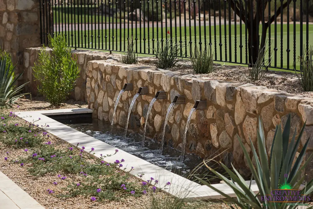 Custom backyard design with metal scupper water feature, natural stone accents and organized planting.