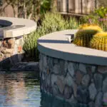 Custom backyard design with curved retention wall, curved pool and water feature into pool.