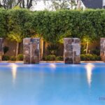 Custom backyard design with privacy hedges and natural stone water columns into pool.
