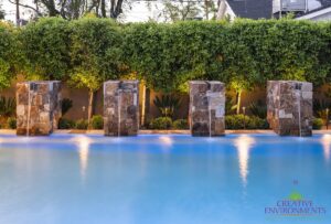 Custom backyard design with privacy hedges and natural stone water columns into pool.