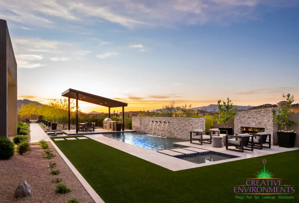 Custom backyard design with natural stone pool wall with metal water feature, Jesus steps and angled shade structure.
