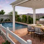 Custom backyard design with white slatted shade structure, water feature into blue pool and outdoor dining area.