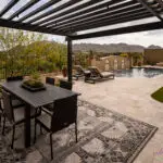 Custom backyard design with slatted metal shade structure, artificial turf and multiple seating areas.