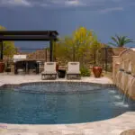Custom backyard design with unique-shaped pool, metal scupper water feature into deco-tile pool and multiple seating areas.
