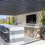 Custom backyard design with slatted metal shade structure, bar seating and large planters.