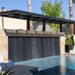 Backyard design with metal cutout shade structure over textured, black water wall into pool.