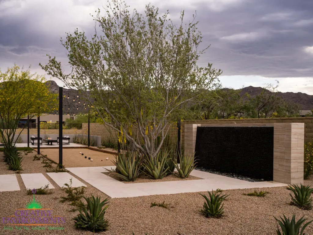 Custom backyard design with black water wall, organized planting and bocce ball court.