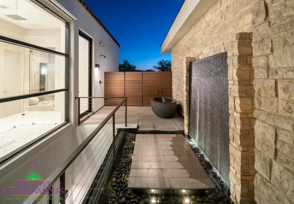 Custom side yard design with outdoor tub, water wall and metal fencing.