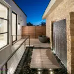 Custom side yard design with outdoor tub, water wall and metal fencing.