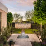 Custom backyard design with water feature, up lighting and artificial turf.