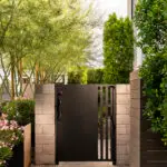 Custom backyard design with metal side gate, privacy hedges and natural stone paver walkway.