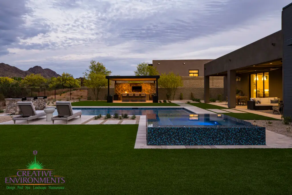 Custom backyard design with raised blue spa, artificial turf and metal shade structure.