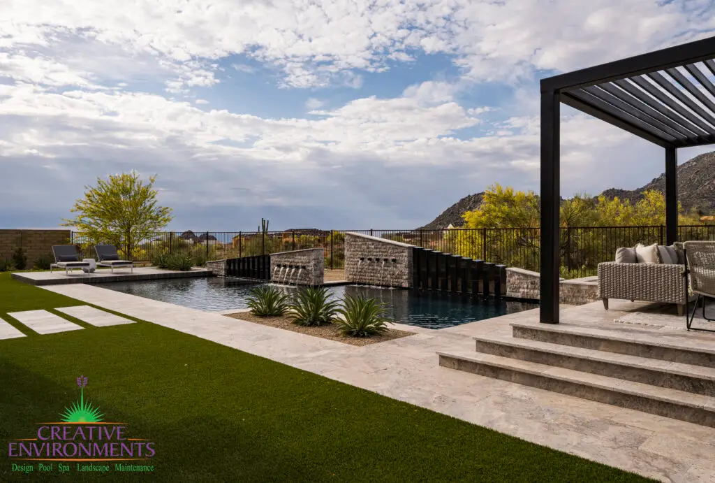 Custom backyard design with multiple water features, raised outdoor entertainment area and artificial turf.