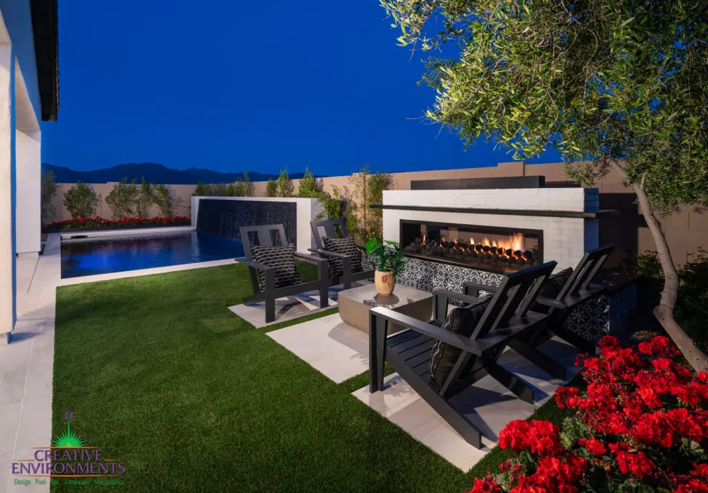 Custom backyard design with deco-tile fireplace, black water wall into pool and artificial turf.