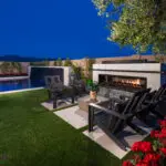 Custom backyard design with deco-tile fireplace, black water wall into pool and artificial turf.