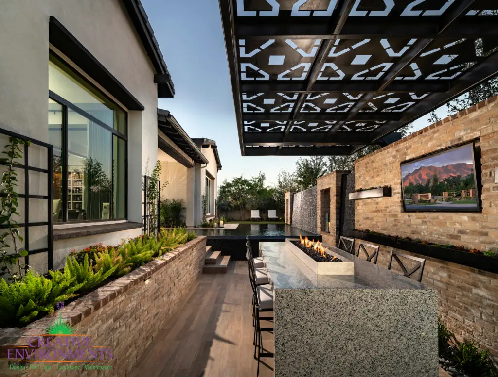 Custom backyard design with cantilevered shade structure with metal cutouts, outdoor TV and fire table.