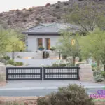 Custom metal entry gate with roundabout driveway and desert landscaping.