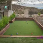 Custom backyard design with bocce ball court, artificial turf and metal fencing.