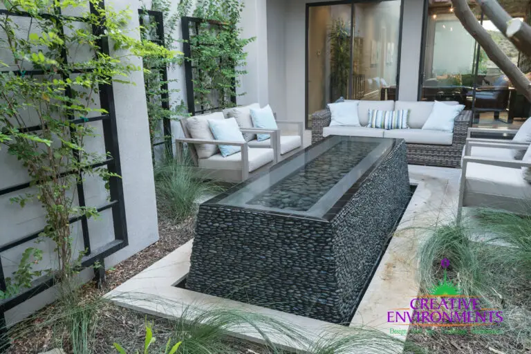 Custom backyard design with metal trellis and black pebble water feature.