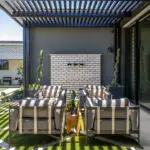 Custom backyard design with slatted metal shade structure, topiaries and artificial turf pattern.