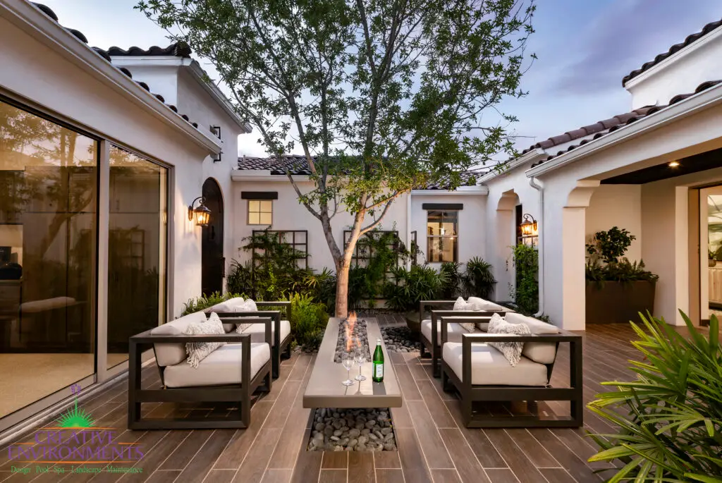 Custom entryway courtyard with large tree, multiple large metal planters and floating fire table.