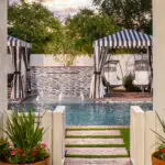 Custom backyard design with water bubbler, pool and multiple cabanas.