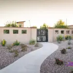 Custom community entrance with metal door, concrete pathway and organized planting.