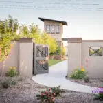 Custom community entrance with metal gate, concrete pathway and organized planting.