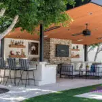 Custom backyard design with angled shade structure, multiple seating areas and real grass.