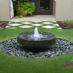 Custom courtyard design with black water feature, artificial turf pattern and black beach pebble stones.