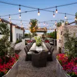 Custom backyard design with string lights, outdoor dining area and multiple planters filled with annuals and small trees.