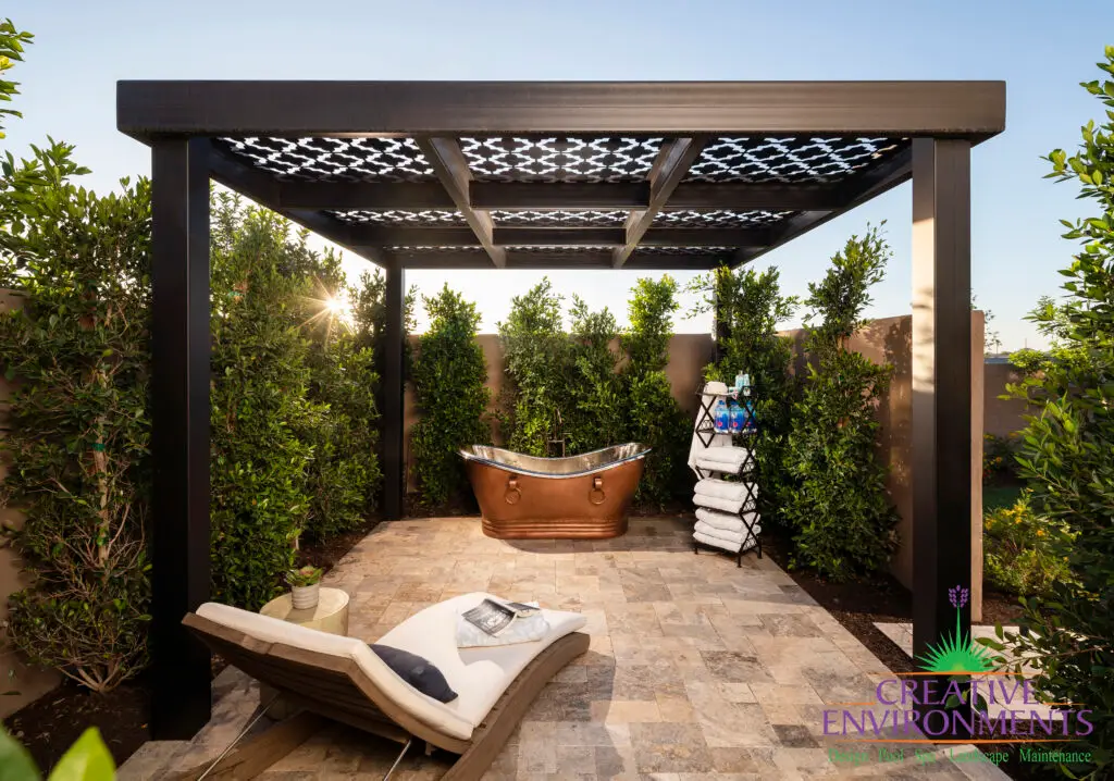 Custom backyard design with patterned metal shade structure, outdoor tub and privacy hedges.