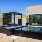 Custom backyard design with black raised spa, slatted metal shade structure and organized planting.