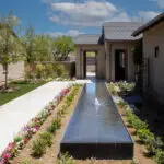 Custom front yard design with black water feature, organized planting and privacy wall.
