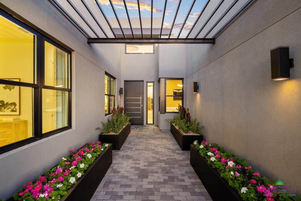 Custom front yard design with linear flower planters, brick paver walkway and outdoor lighting.